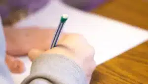 Aluno escrevendo com lápis em prova