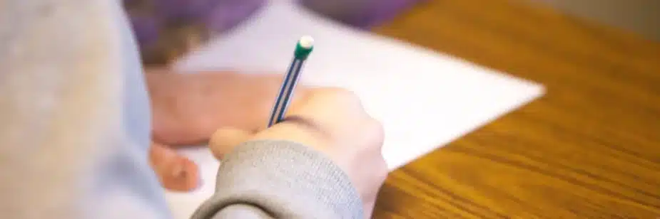 Aluno escrevendo com lápis em prova
